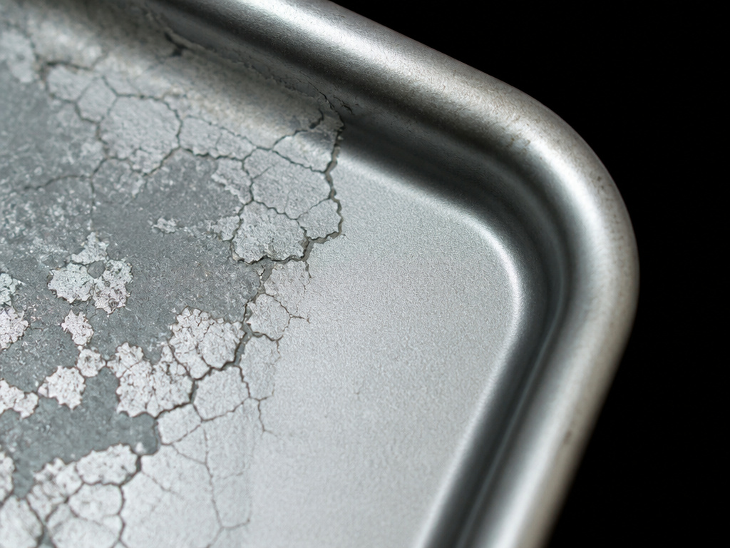 Aluminized steel bakeware coating degradation under thermal stress close-up.