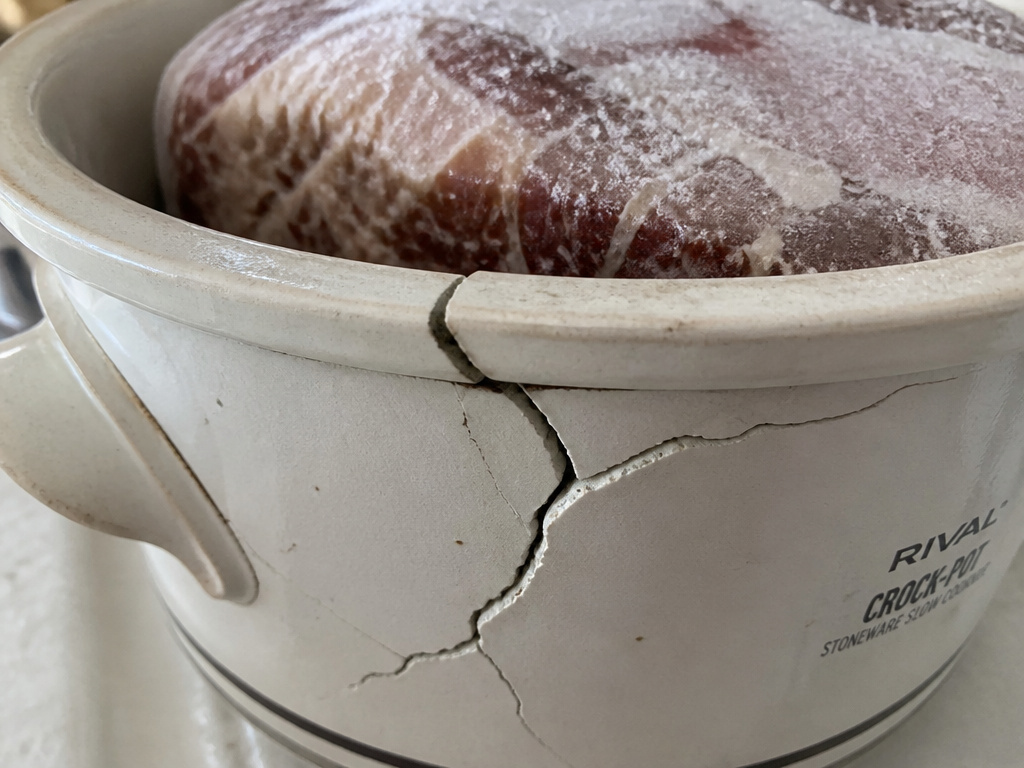Cracked ceramic slow cooker pot with a frozen roast inside due to thermal shock