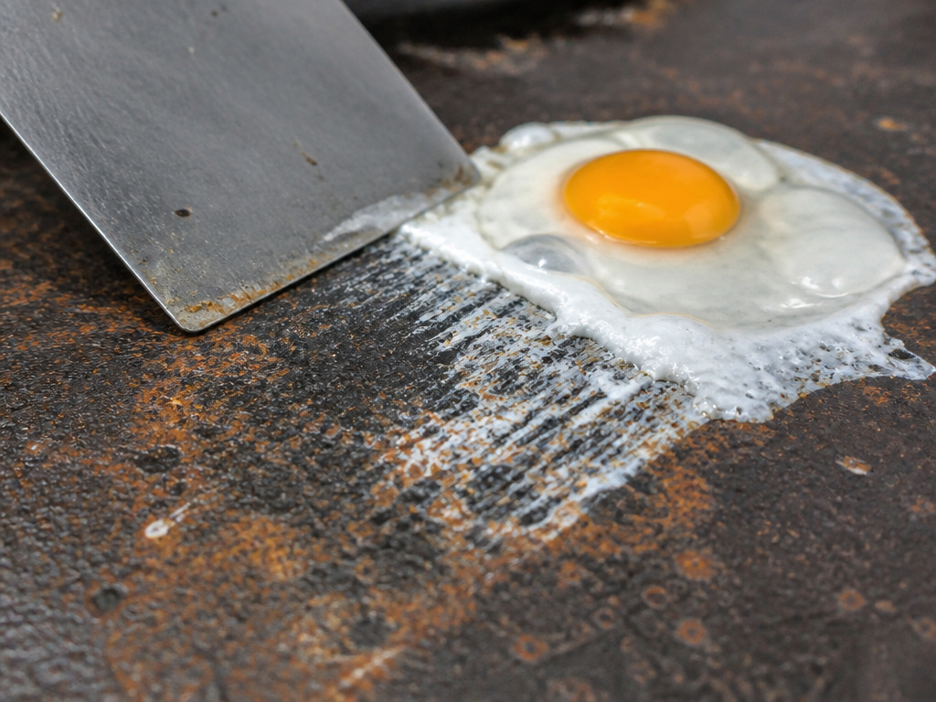 Rusty unseasoned griddle surface with stuck egg and scraping damage
